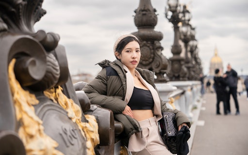 Person posing on Pont Alexandre III bridge in Paris with ornate lampposts in the background.