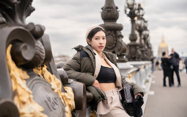 Person posing on Pont Alexandre III bridge in Paris with ornate lampposts in the background.