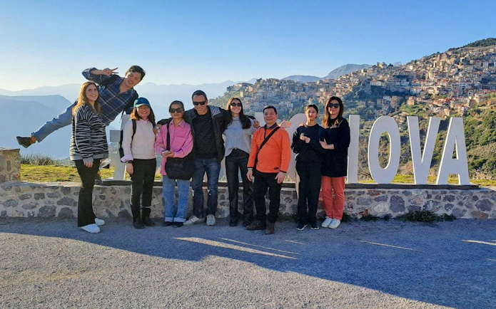 Tour group posing by Arachova sign with Delphi in the background, Greece.