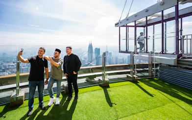 Tourists taking photos on Kuala Lumpur Tower Sky Terrace with city skyline view.