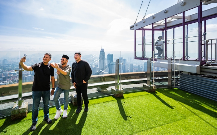 Tourists taking photos on Kuala Lumpur Tower Sky Terrace with city skyline view.