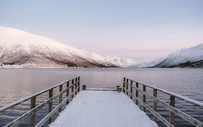 Snow-covered pier overlooking Sommarøy Fjord with snowy mountains, Tromsø.
