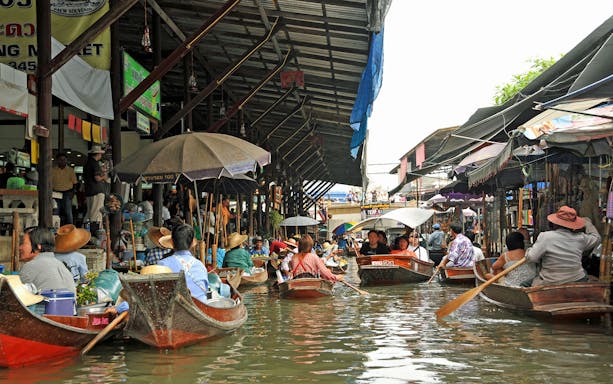 Boats navigating Damnoen Saduak Floating Market, Thailand, with vendors selling goods.