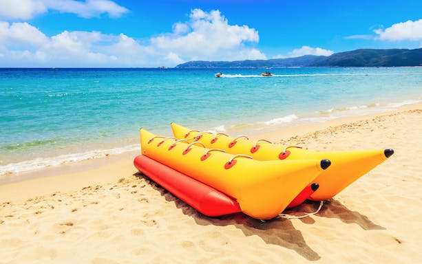 Yellow banana boat on sandy beach with ocean and distant jet skis.