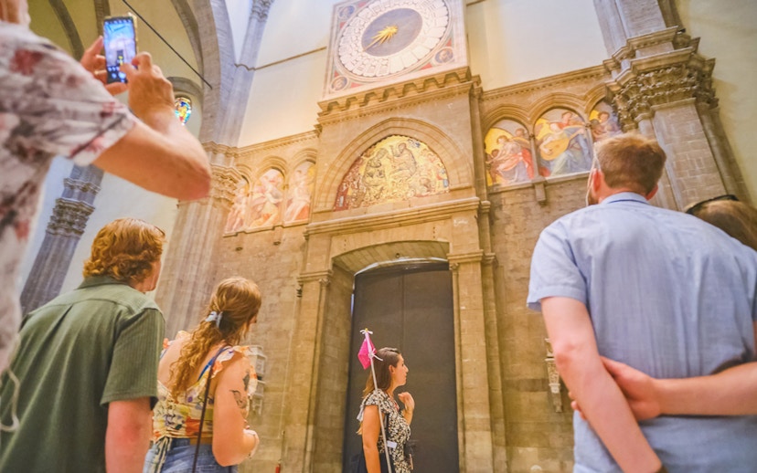Tour group observing frescoes and clock inside Florence Cathedral.