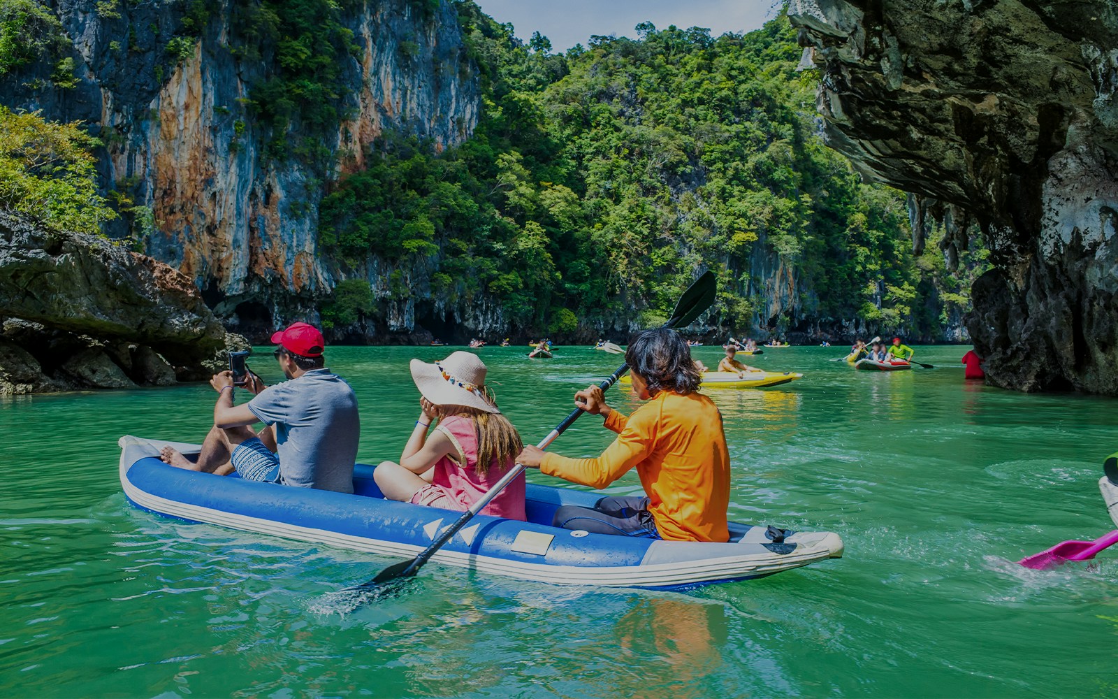 Group kayaking in Thailand's turquoise waters near limestone cliffs.