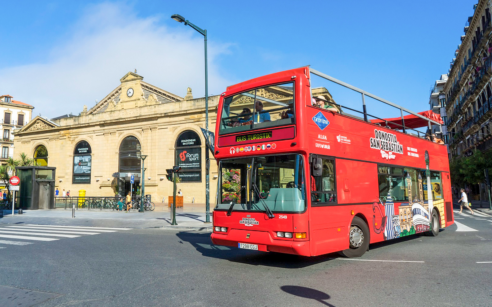 Red double-decker bus on San Sebastian city tour near historic building.