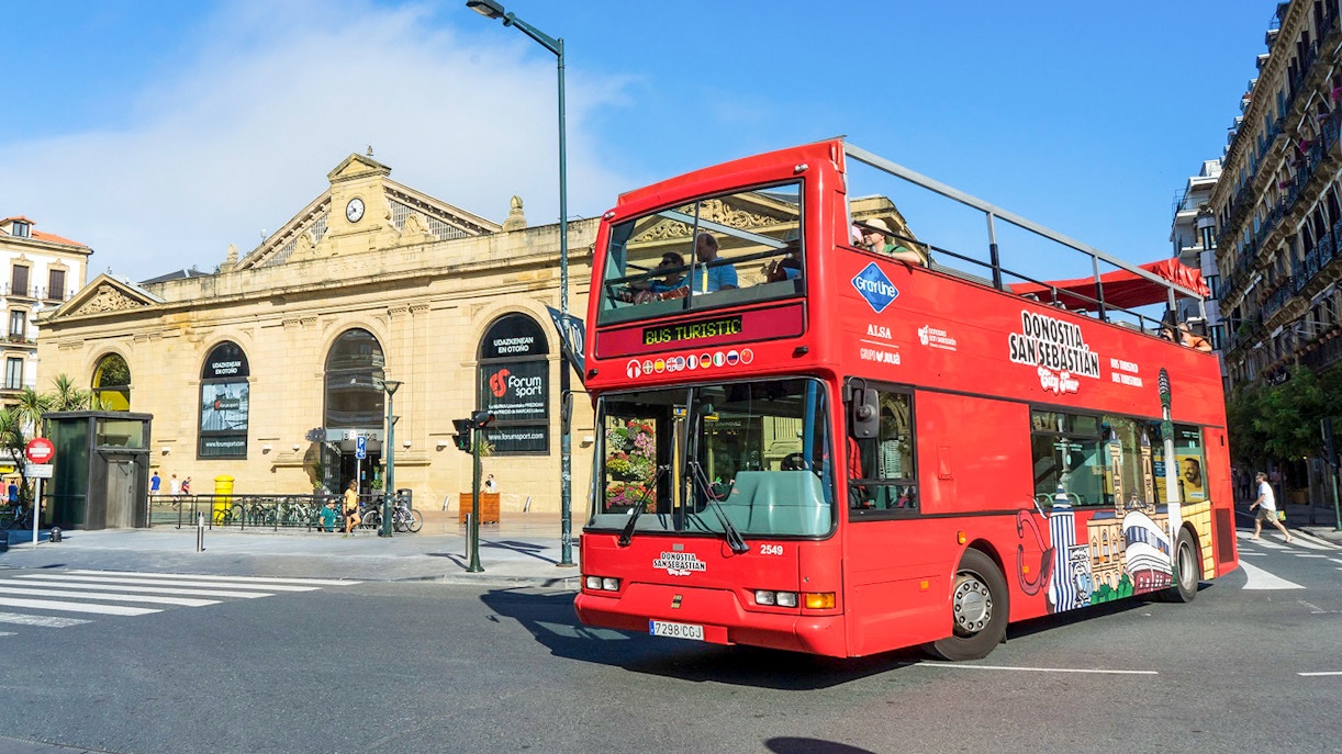 Roter Doppeldeckerbus auf Stadtrundfahrt in San Sebastián in der Nähe eines historischen Gebäudes.