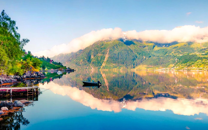 Hardangerfjord in Norway with mountains and clouds reflected in calm water.