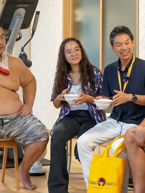 Sumo wrestlers and visitors sharing a meal during a morning practice in a sumo stable.