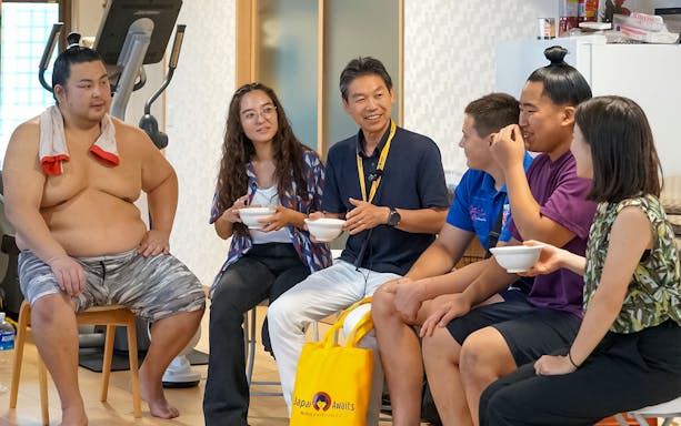 Sumo wrestlers and visitors sharing a meal during a morning practice in a sumo stable.