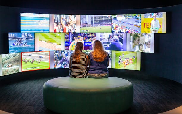 Visitors viewing sports highlights at Australian Sports Museum screen display.
