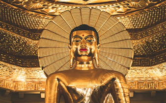 Golden Buddha statue with intricate halo and ornate ceiling details.