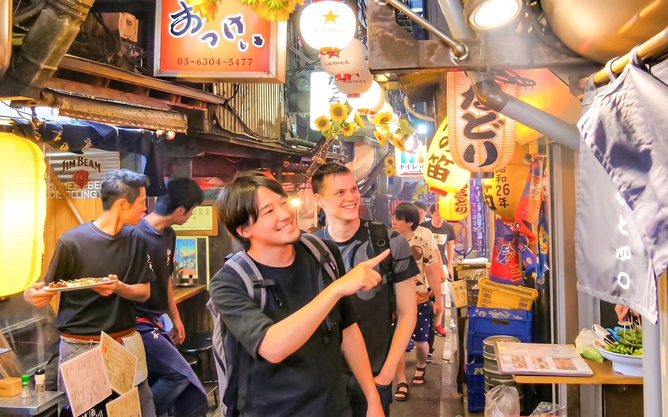 Tourists exploring vibrant alleyways of Golden Gai, Shinjuku with lanterns and signs.
