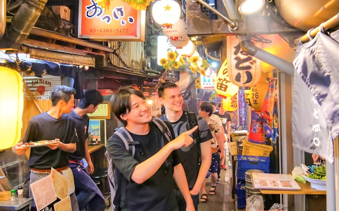Tourists exploring vibrant alleyways of Golden Gai, Shinjuku with lanterns and signs.