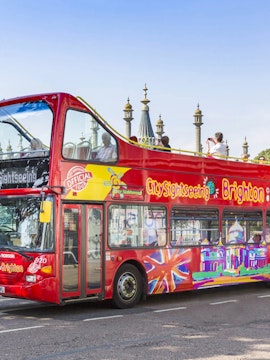 Brighton hop-on hop-off bus near Royal Pavilion with tourists on top deck.