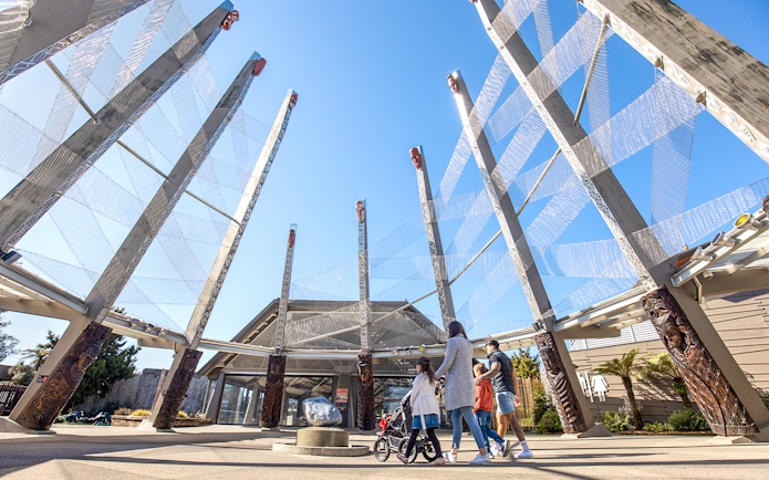 Visitors exploring Te Puia entrance with carved wooden pillars, Rotorua, New Zealand.