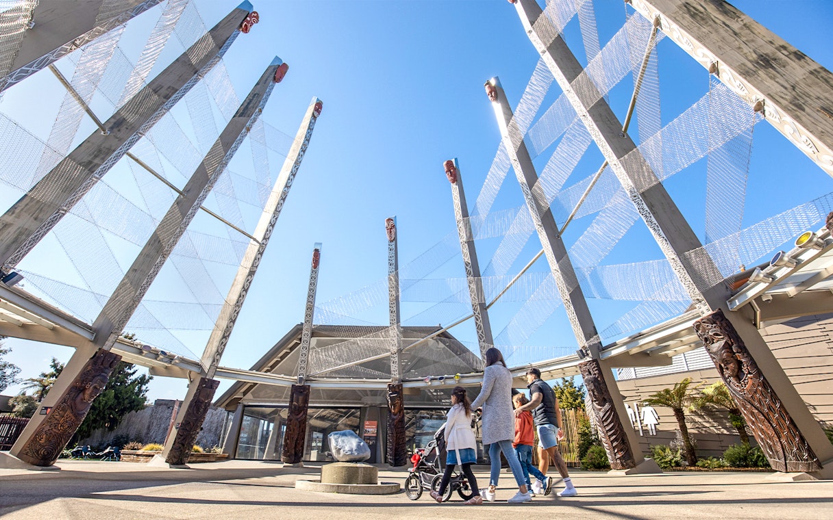 Visitors exploring Te Puia entrance with carved wooden pillars, Rotorua, New Zealand.