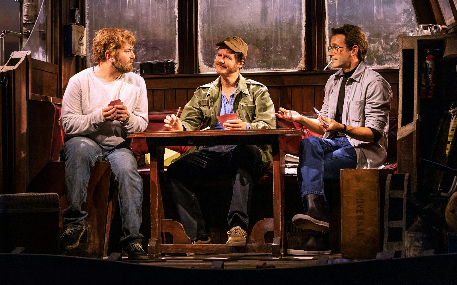 Three actors sitting at a table on a stage set for "The Shark is Broken" play.