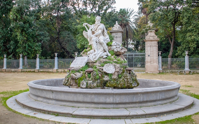 Statue in Orto Botanico garden, Palermo, surrounded by greenery and stone fence.