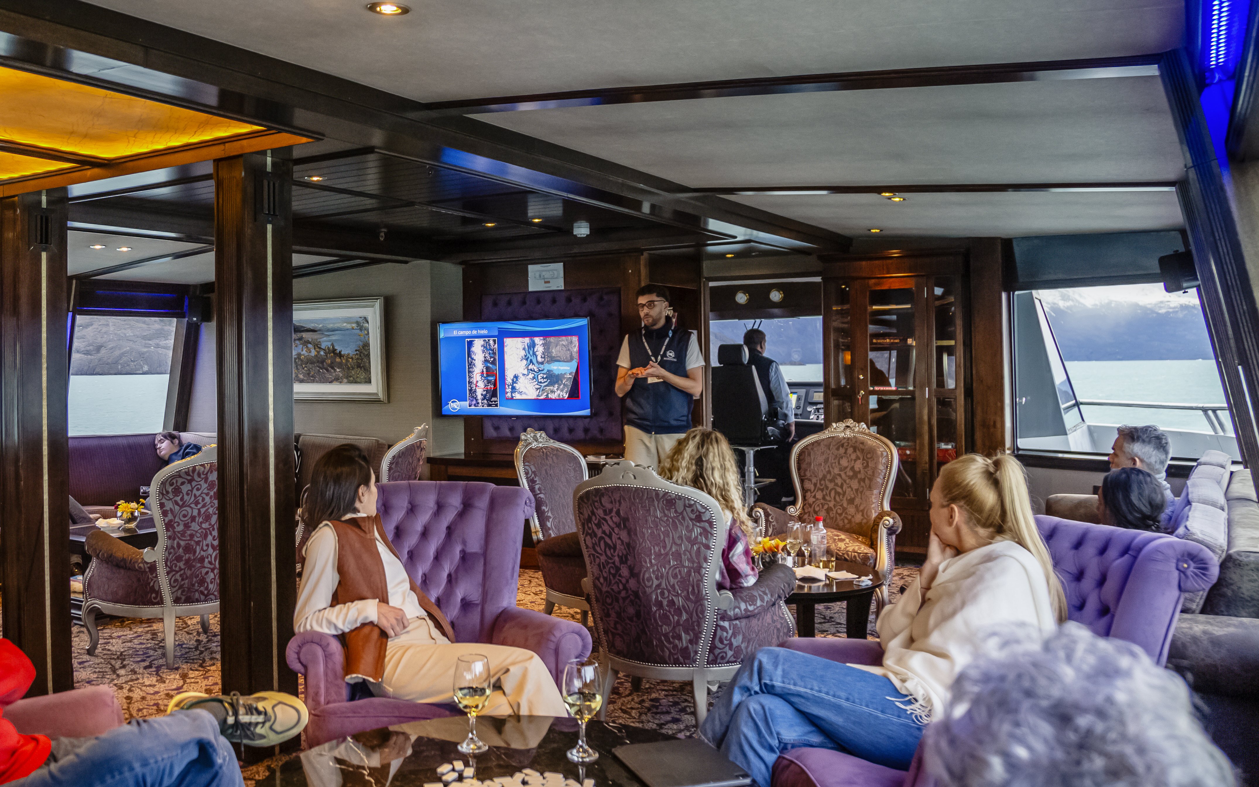 Lounge area on boat with passengers during Spirit of the Glaciers tour, featuring a presentation.