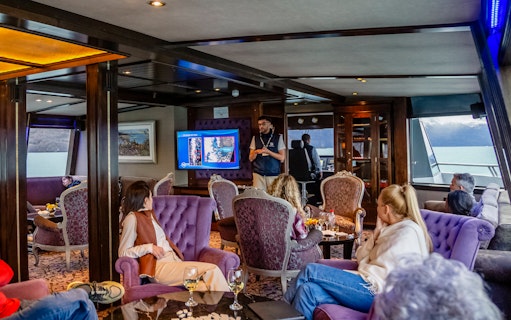 Lounge area on boat with passengers during Spirit of the Glaciers tour, featuring a presentation.