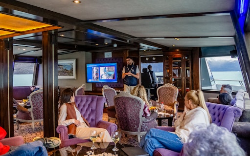 Lounge area on boat with passengers during Spirit of the Glaciers tour, featuring a presentation.