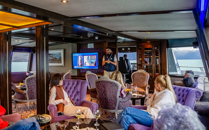 Lounge area on boat with passengers during Spirit of the Glaciers tour, featuring a presentation.