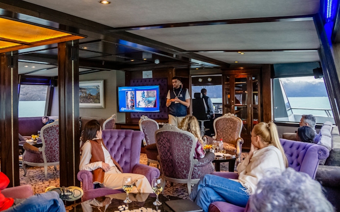 Lounge area on boat with passengers during Spirit of the Glaciers tour, featuring a presentation.