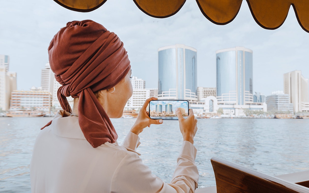 Woman photographing skyline from Abra Dhow boat on Dubai Creek.