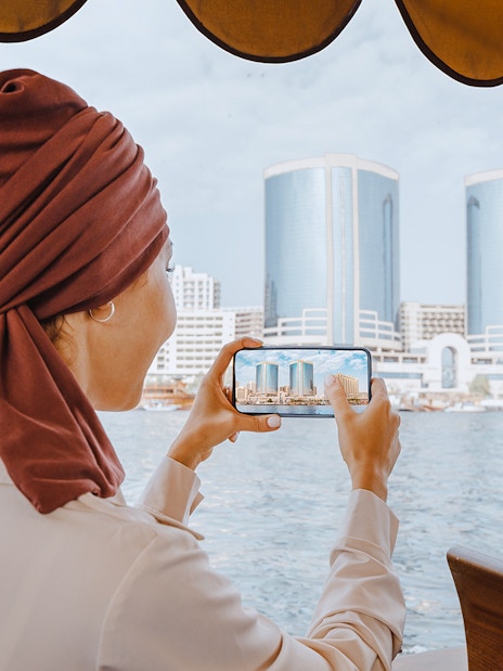 Woman photographing skyline from Abra Dhow boat on Dubai Creek.