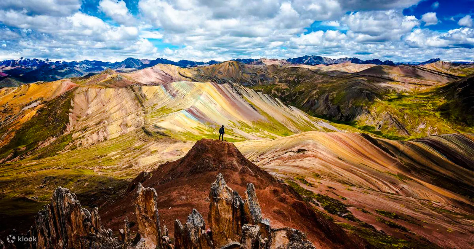 Person standing on a hill overlooking the colorful Palcoyo Rainbow Mountain in Cusco, Peru.