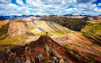 Person standing on a hill overlooking the colorful Palcoyo Rainbow Mountain in Cusco, Peru.