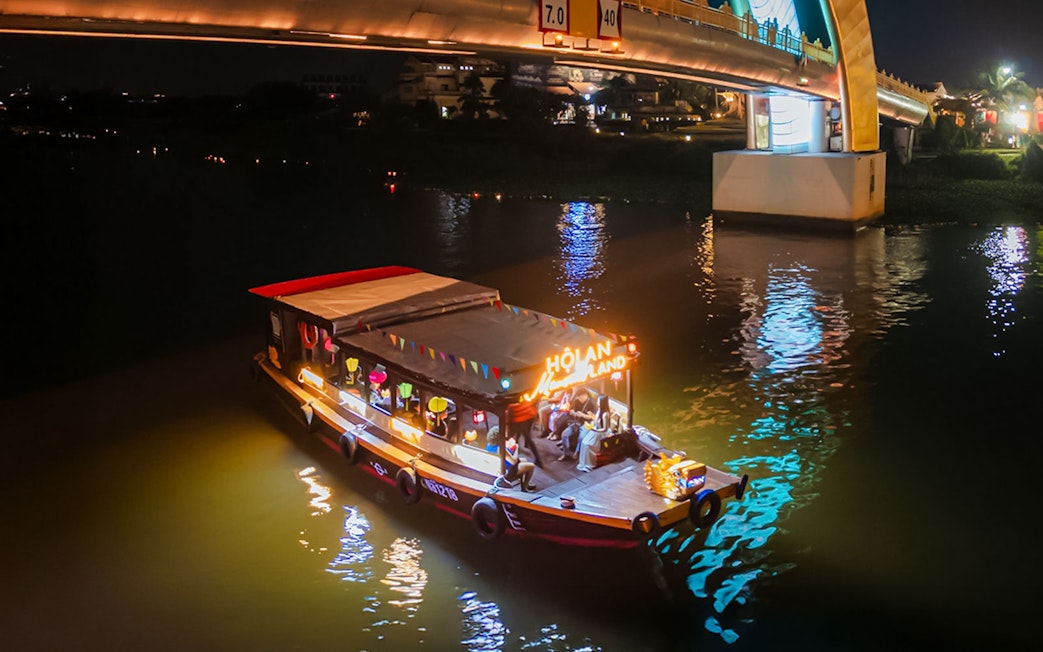 Hoi An river cruise boat illuminated at night under a lit bridge.