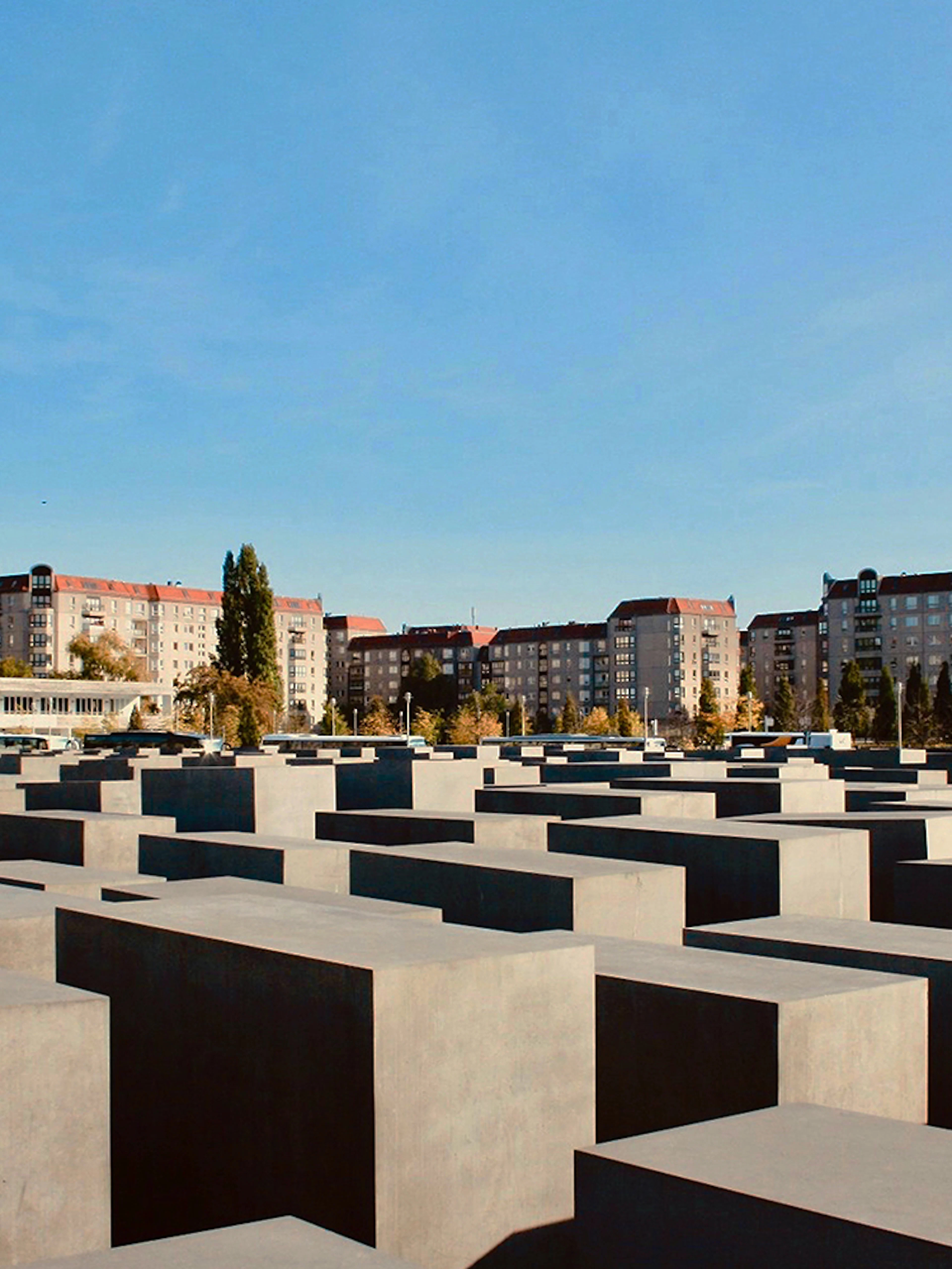 Holocaust Memorial in Berlin with concrete slabs and city buildings in the background.