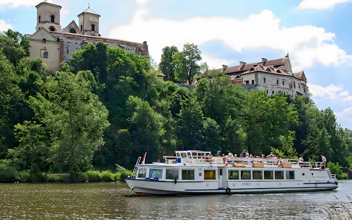 Sightseeing boat on Vistula River near historic monastery in Krakow, Poland.