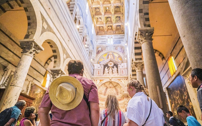 Visitors inside Pisa Cathedral, Italy, admiring ornate ceiling and arches.