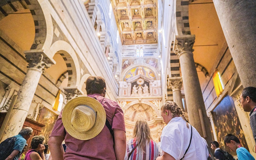 Visitors inside Pisa Cathedral, Italy, admiring ornate ceiling and arches.