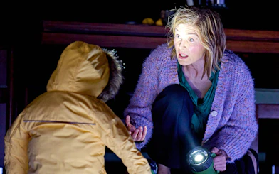 Broadway Inter Alia show scene with woman holding flashlight, engaging with child in yellow coat.