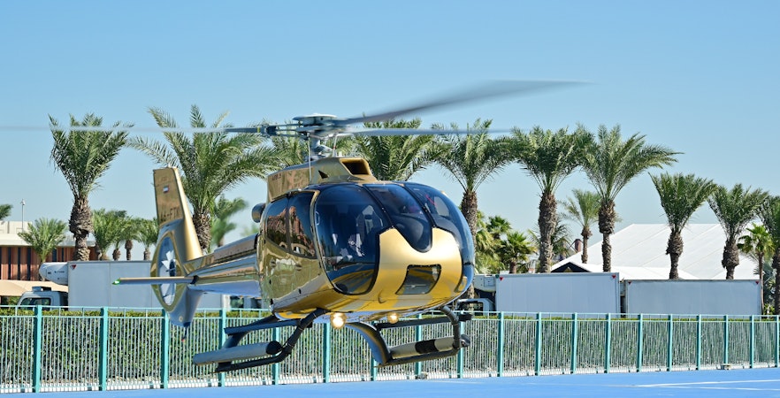 Helicopter on helipad ready for Dubai aerial tour with palm trees in background.