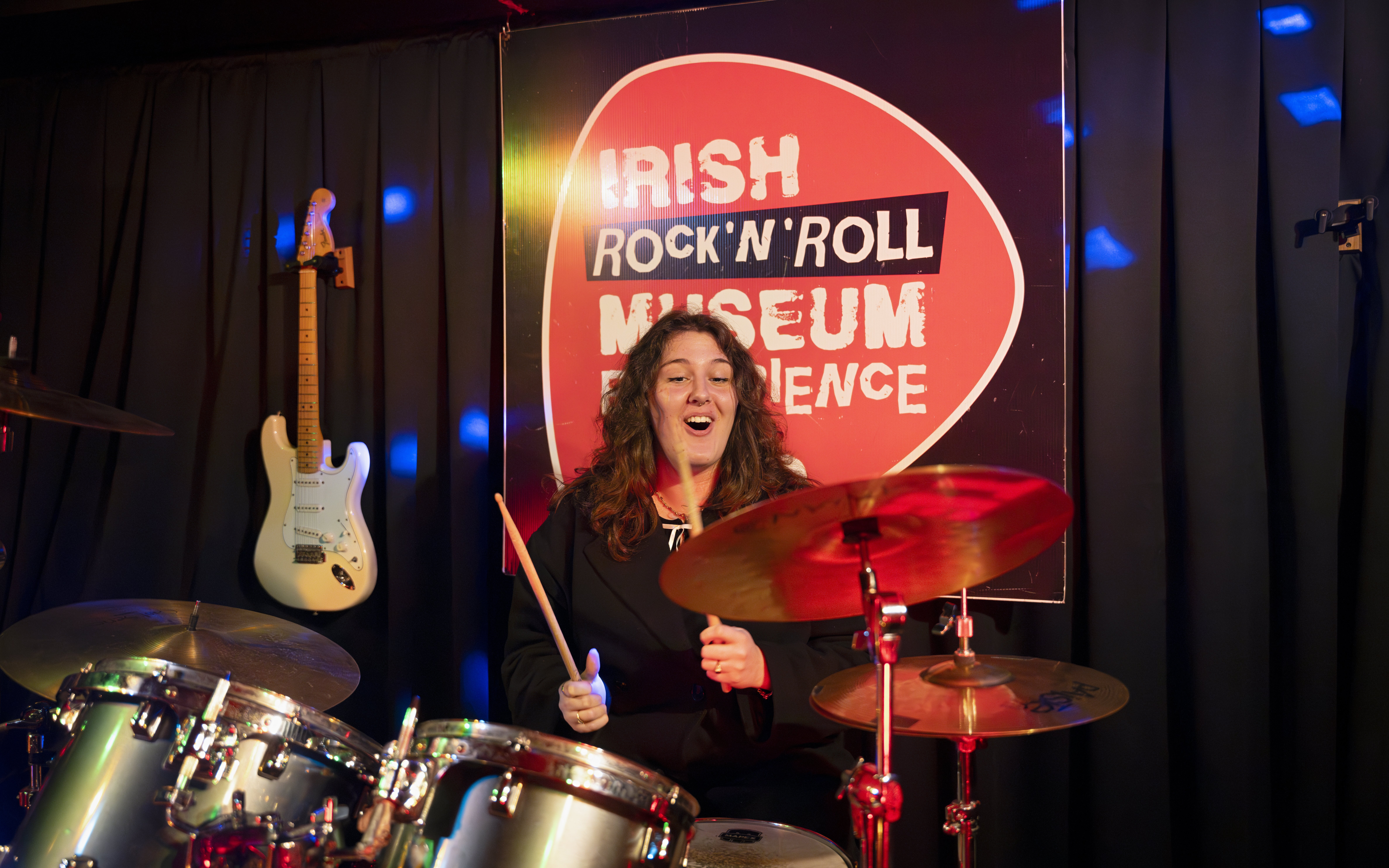Drummer performing at Irish Rock N Roll Museum Experience with guitar on display.