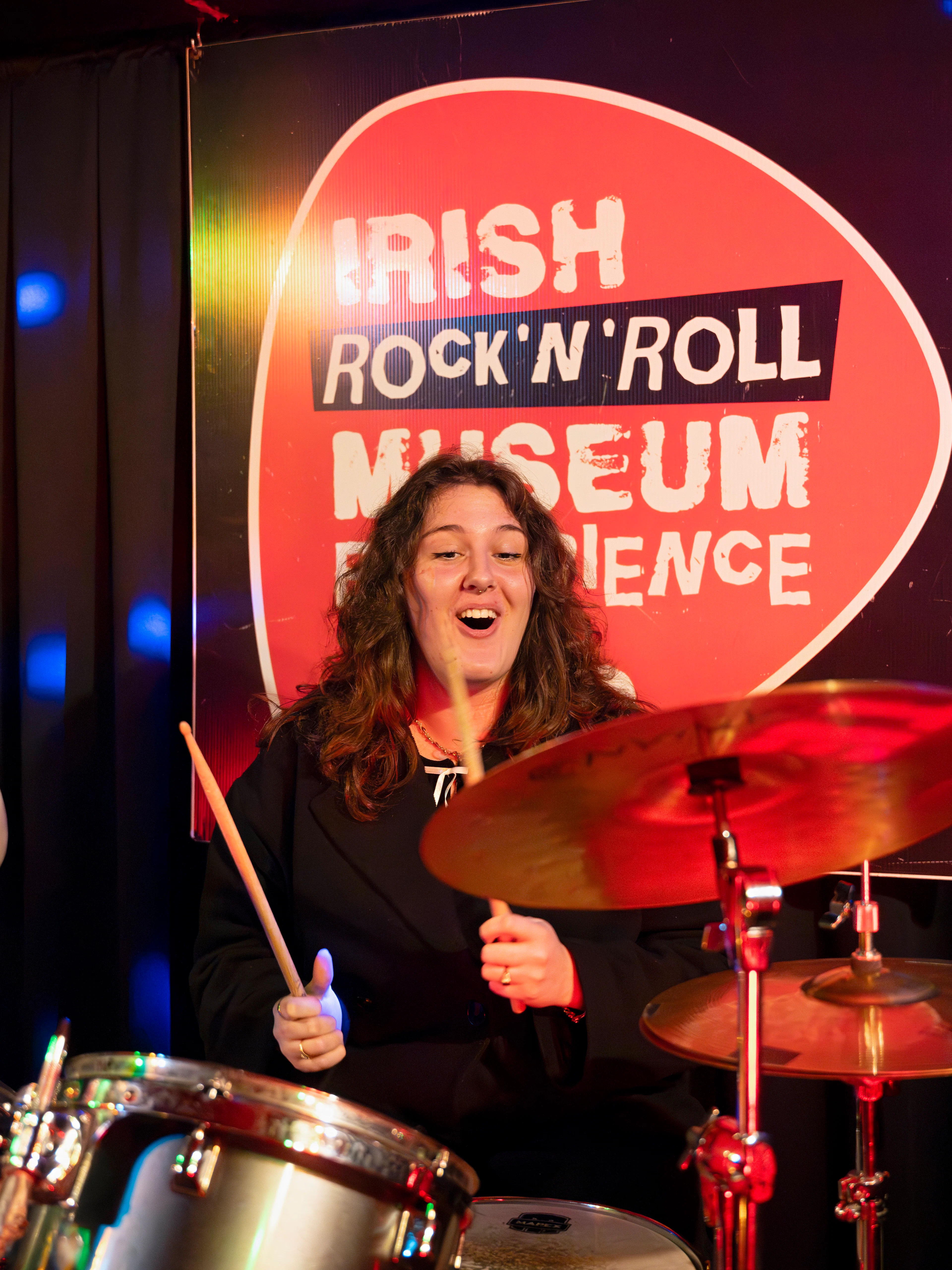 Drummer performing at Irish Rock N Roll Museum Experience with guitar on display.