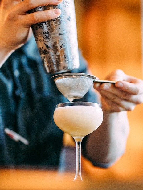 Bartender straining cocktail into glass at Roe & Co Distillery.