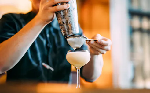 Bartender straining cocktail into glass at Roe & Co Distillery.