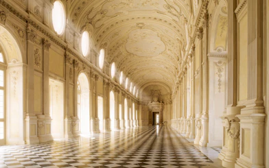 Grand hallway in Turin's Royal Palace with ornate ceiling and checkered floor.