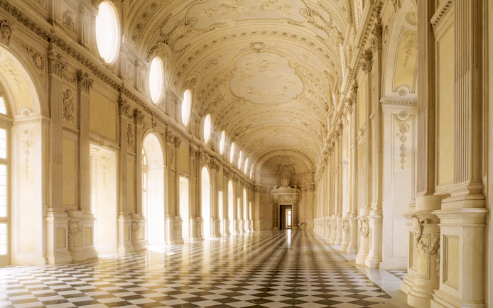 Grand hallway in Turin's Royal Palace with ornate ceiling and checkered floor.