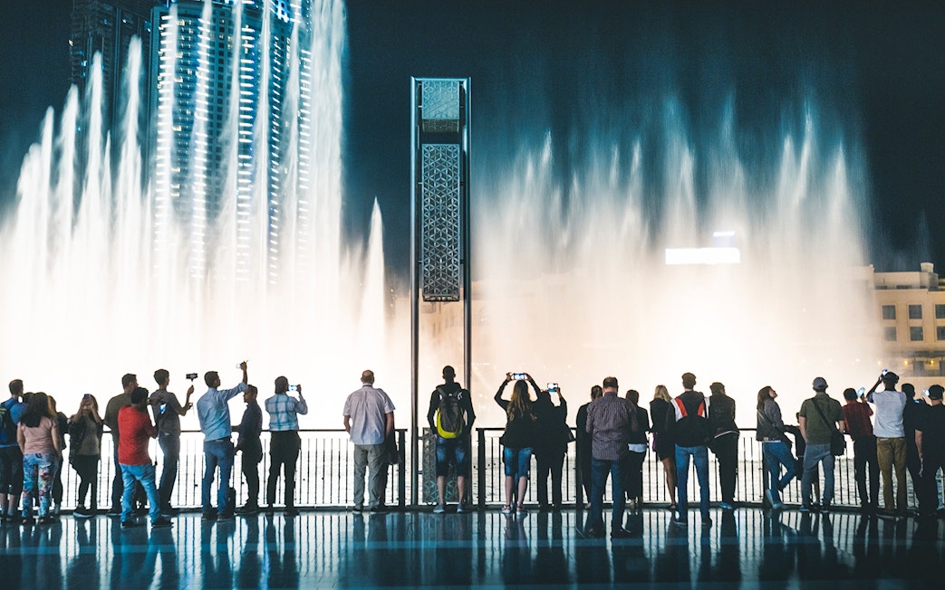 Visitors watching Dubai Fountain show from boardwalk at night.