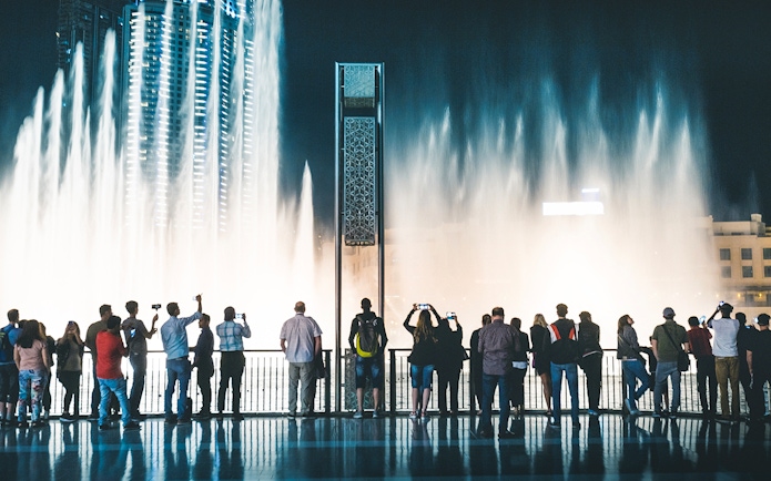 Visitors watching Dubai Fountain show from boardwalk at night.