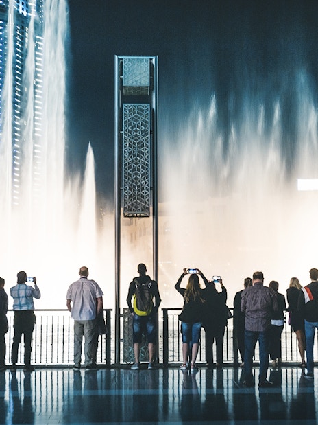 Visitors watching Dubai Fountain show from boardwalk at night.
