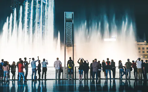 Visitors watching Dubai Fountain show from boardwalk at night.
